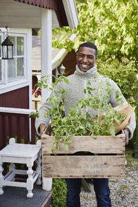 Smiling man holding crate with tomato plants