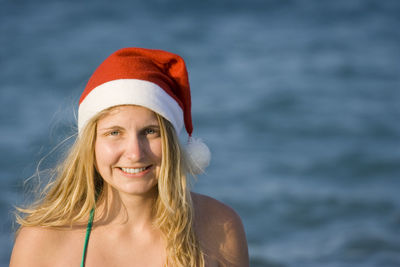 Portrait of young woman wearing santa hat against sea