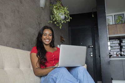 Young black woman working at home with laptop on her lap sitting on her couch  notebook for working. 