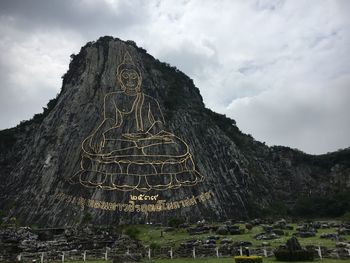 Buddha sculpture on mountain against cloudy sky
