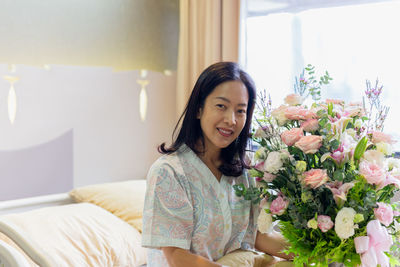Woman patient smiling and holding a flower bouquet sitting on hospital bed.
