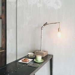 Breakfast on table by illuminated light bulb against wall