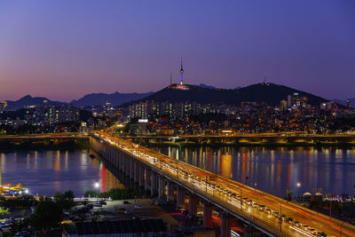 Illuminated bridge over river amidst buildings in city at night