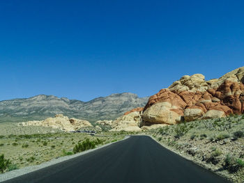 Road leading towards mountains against clear blue sky