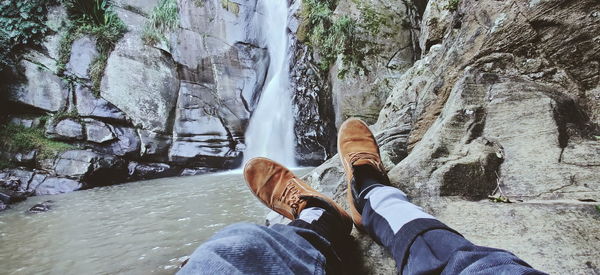 Low section of man standing on rock against waterfall