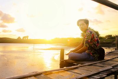 Woman sitting on land against sky during sunset