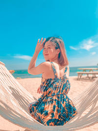 Woman looking away while sitting on hammock against sky