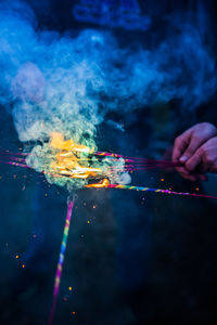 Cropped hands holding lit sparklers at night