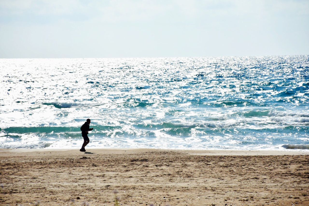 MAN STANDING ON SHORE AGAINST SKY