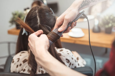 Hair stylist barber styling long hair with hair iron for beautiful young woman in beauty salon