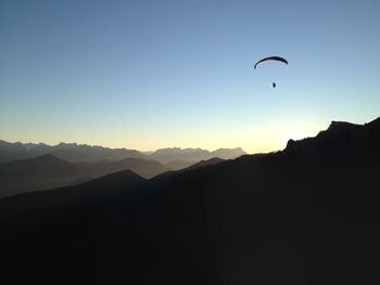 Silhouette person paragliding against clear sky during sunset