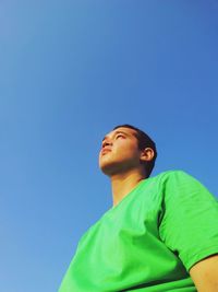 Low angle view of young man looking away against clear blue sky