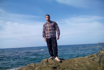Full length of man standing on rock by sea against sky