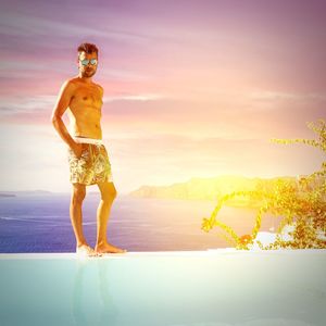 Full length of shirtless man standing by sea against sky