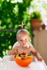 Boy holding fruit salad in bowl on table