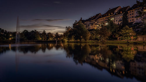 Scenic view of lake by buildings against sky at night