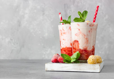 Strawberry and raspberry smoothies in glasses garnish with mint and raspberry on wooden board.