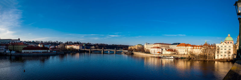 Buildings by river against blue sky