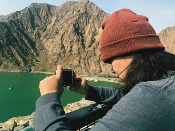 Side view of woman photographing with mobile phone against mountains