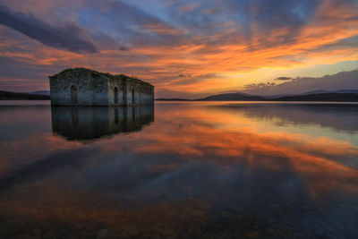 Old house in lake against cloudy sky