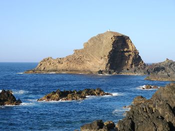 Scenic view of rocks in sea against clear blue sky