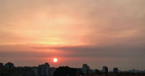 Silhouette of city against cloudy sky during sunset