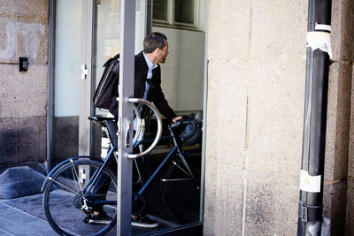 Businessman with bicycle entering doorway in city