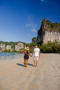 Rear view of women on rock formation at beach against sky