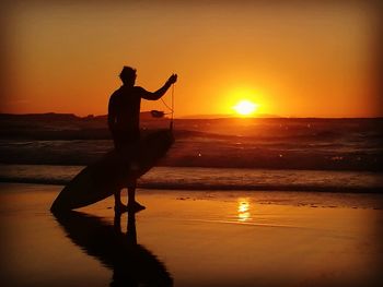 Side view of silhouette man standing at beach during sunset