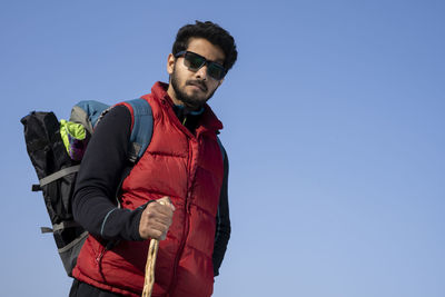 Low angle view of young man standing against clear blue sky