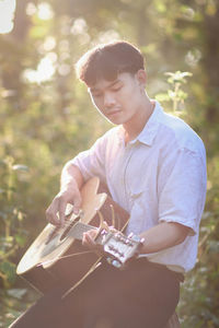 Young man playing guitar against plants