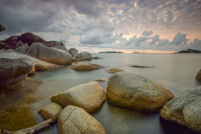 Rocks at sea shore against sky during sunset