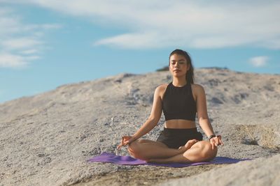 Portrait of young woman sitting on rock against sky