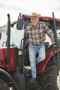 Portrait of smiling senior farmer getting out of tractor