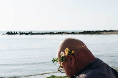 Close-up of bald man wearing flowers against sea