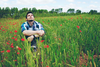 Thoughtful mid adult man hugging knees while sitting amidst plants on field