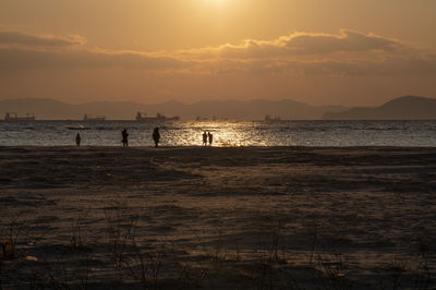 Silhouette people on beach against sky during sunset