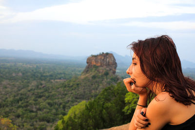 Side view of young woman looking at mountain against sky