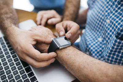 Adult grandson teaching his grandfather to use smartwatch, close-up