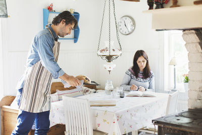 Side view of man serving bread on dining table for woman at home