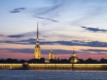 View of building by river against sky during sunset