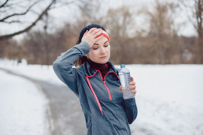 Tired woman wearing sports clothing having water on road during winter