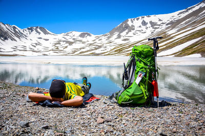 People sitting on snow covered mountain by lake against sky