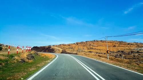 Road passing through mountains against clear blue sky