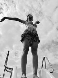 Low angle view of woman with arms outstretched standing on slide against sky