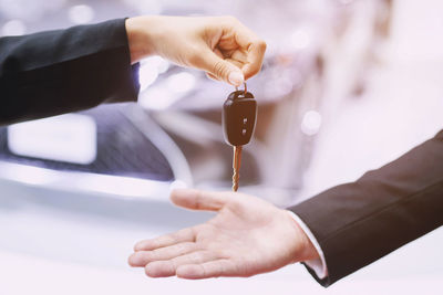 Cropped hand of man giving key to person with car on road in background