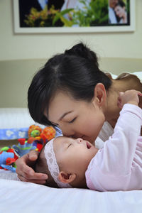 Mother playing with baby girl lying on bed at home