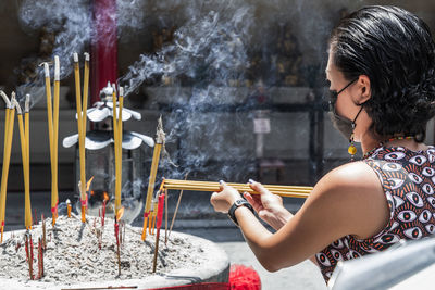 Side view of woman holding incense at temple