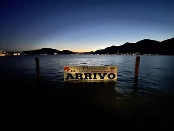 Information sign by lake against sky at night