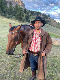 Side view of latin man standing with his horse in a field in montana